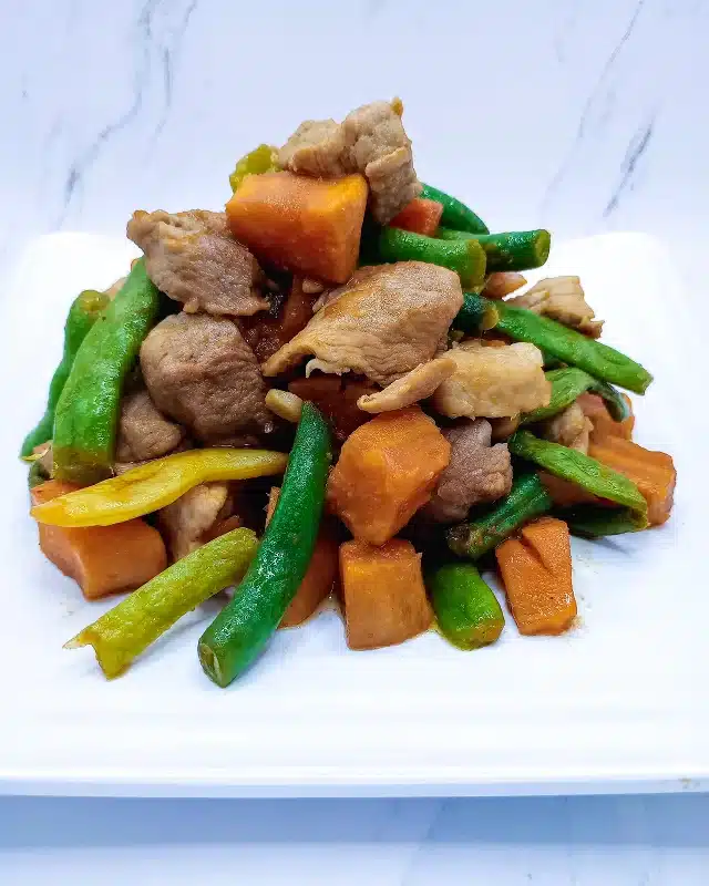 A finished bowl of pork and green beans stir fry with a drizzle of soy sauce.