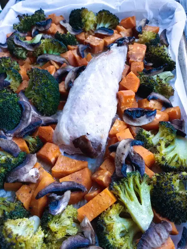 pork loin, sweet potatoes, broccoli, and mushrooms on a sheet pan after being baked and removed from the oven