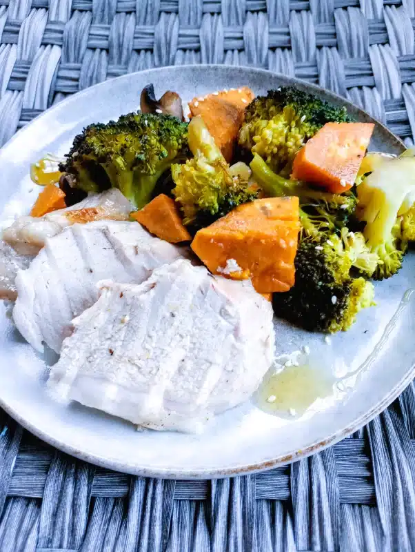 pork loin slices served on a white plate with broccoli, sweet potatoes, and mushrooms to the side